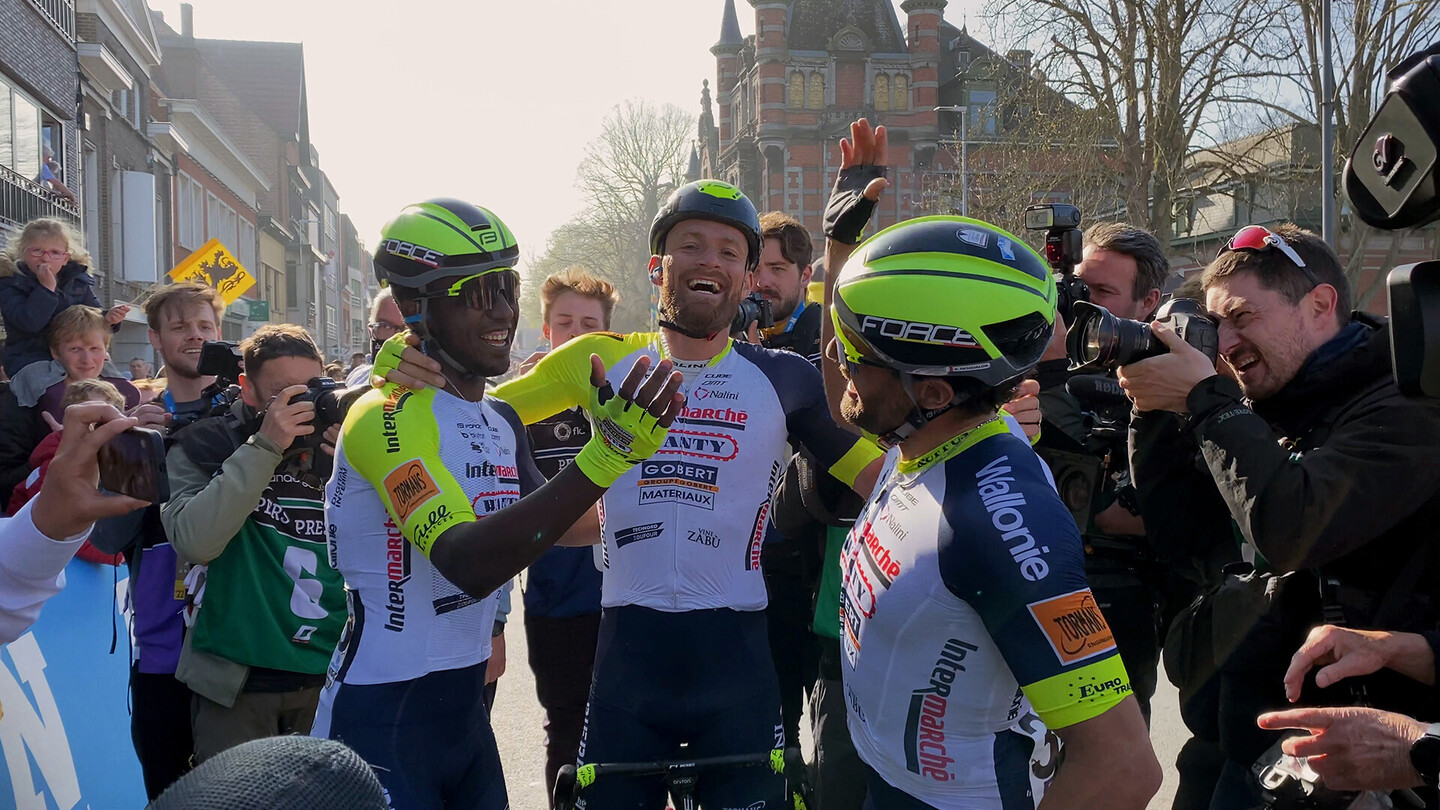 Wegwielrenners vieren hun overwinning bij de finish, omringd door fotografen en fans.